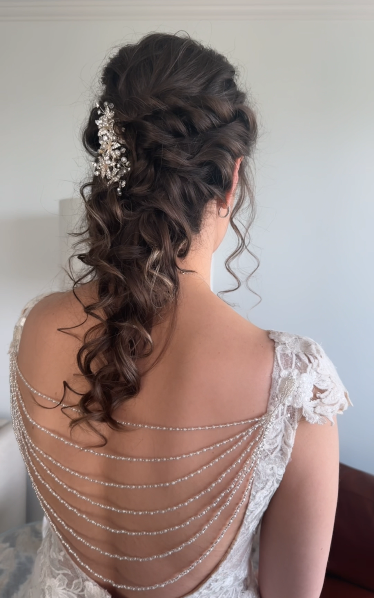 Bride with intricate hairpiece and lace backless dress against a plain background