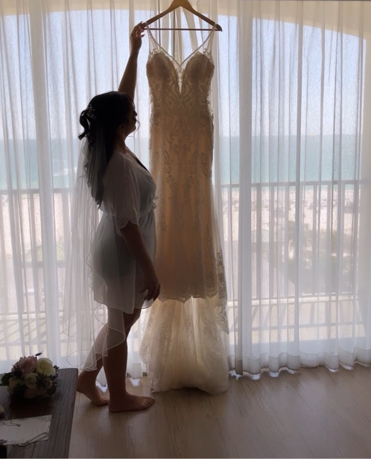 Woman holding a wedding dress in front of sheer curtains