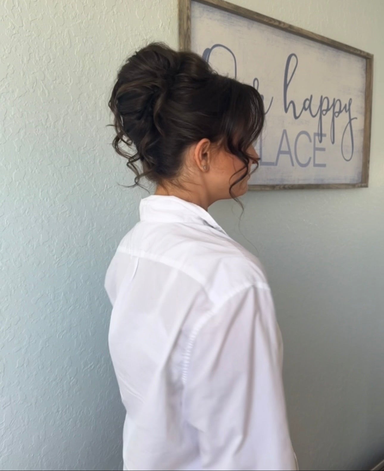 Woman with styled hair in a room with a framed sign on the wall.
