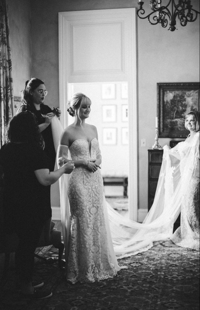 Black and white wedding morning photo of bride getting ready in her gown by Glow & Go Beauty